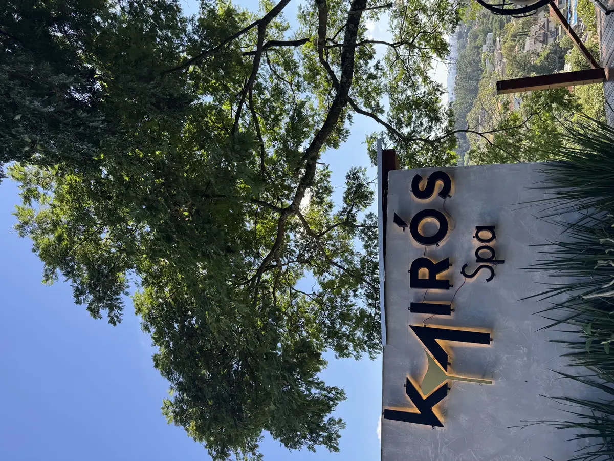 Placa do Kairós Spa com logo em destaque sob árvore frondosa e céu azul ao fundo